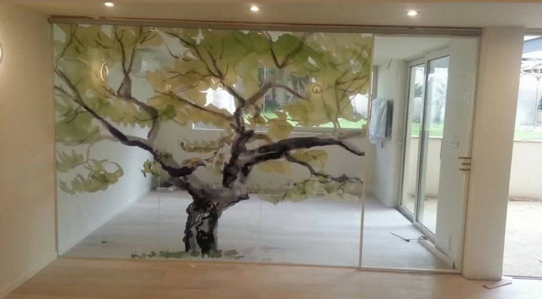 A painted tree extends across a glass wall, bringing branches and leaves into the architecture.